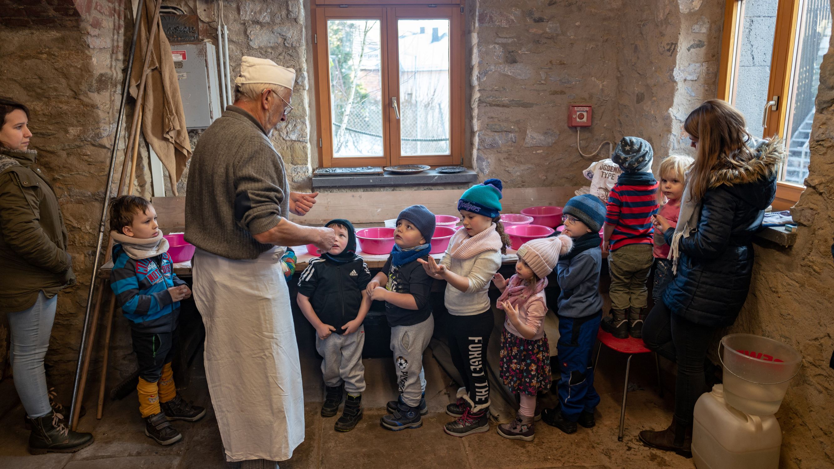 Bäcker steht mit acht Kindern in einer Backstube