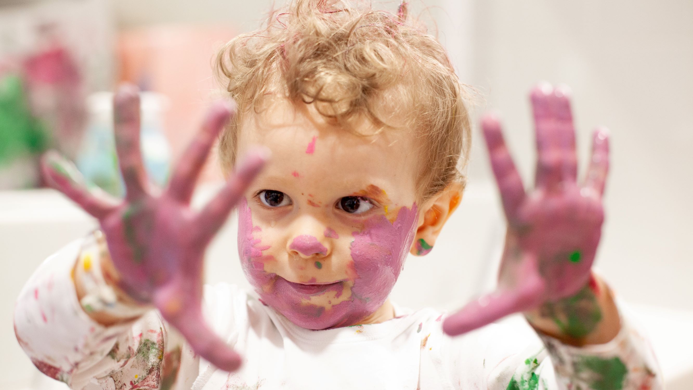 Ein Kind zeigt seine mit rosa Farbe beschmierten Hände