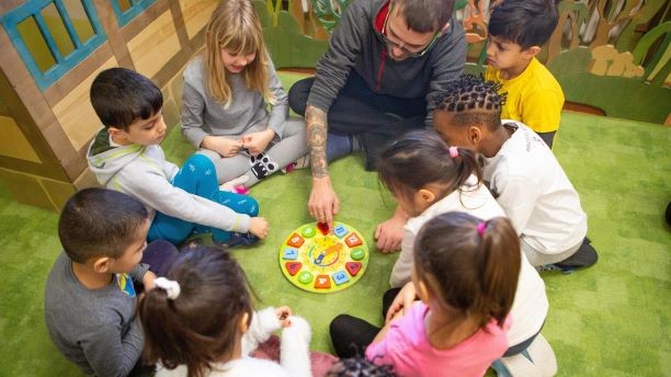 Kita-Kinder sitzen im Kreis und lernen eine Uhr zu lesen