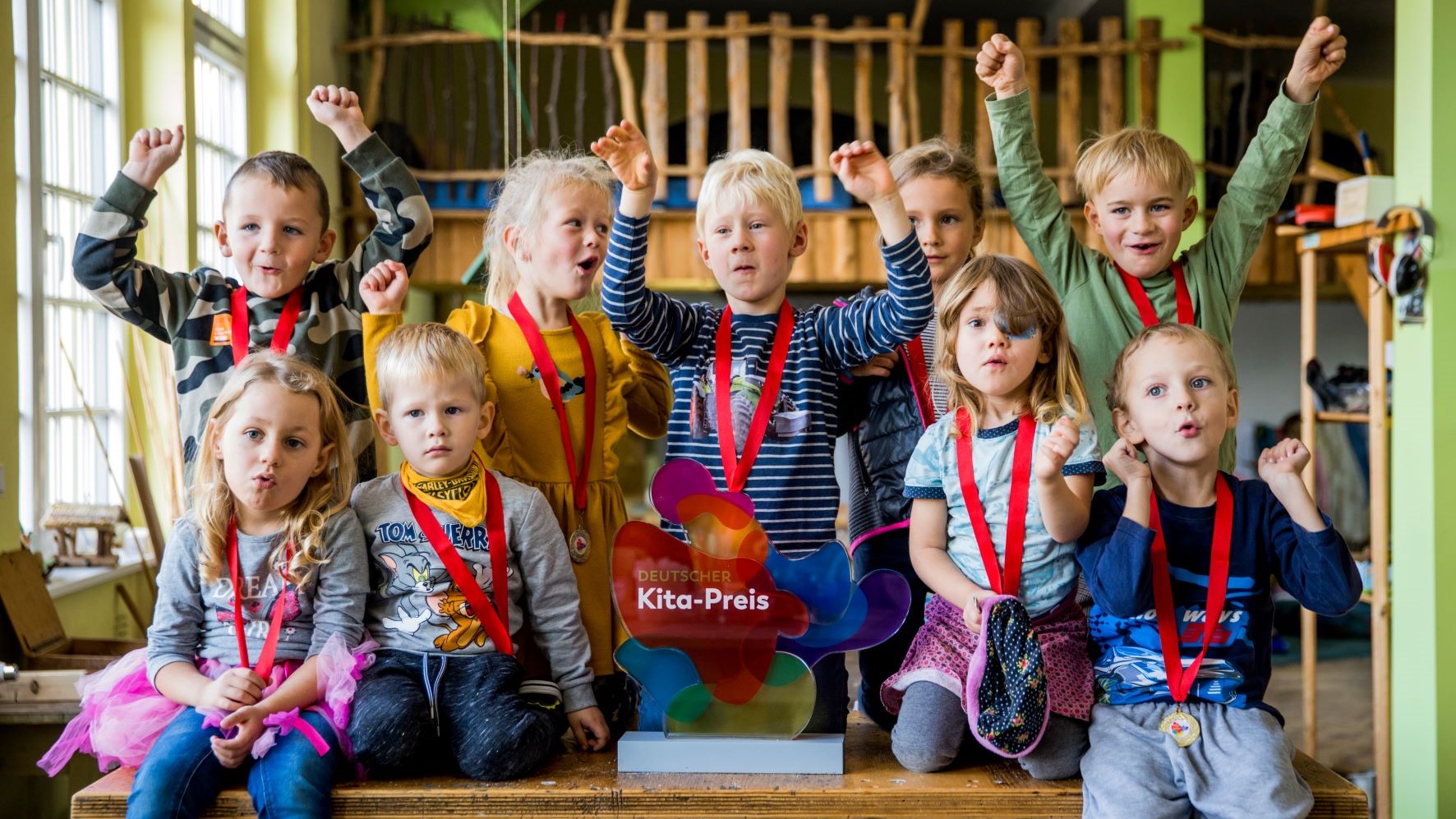 Kinder jubeln neben der Trophäe des Deutschen Kita-Preises