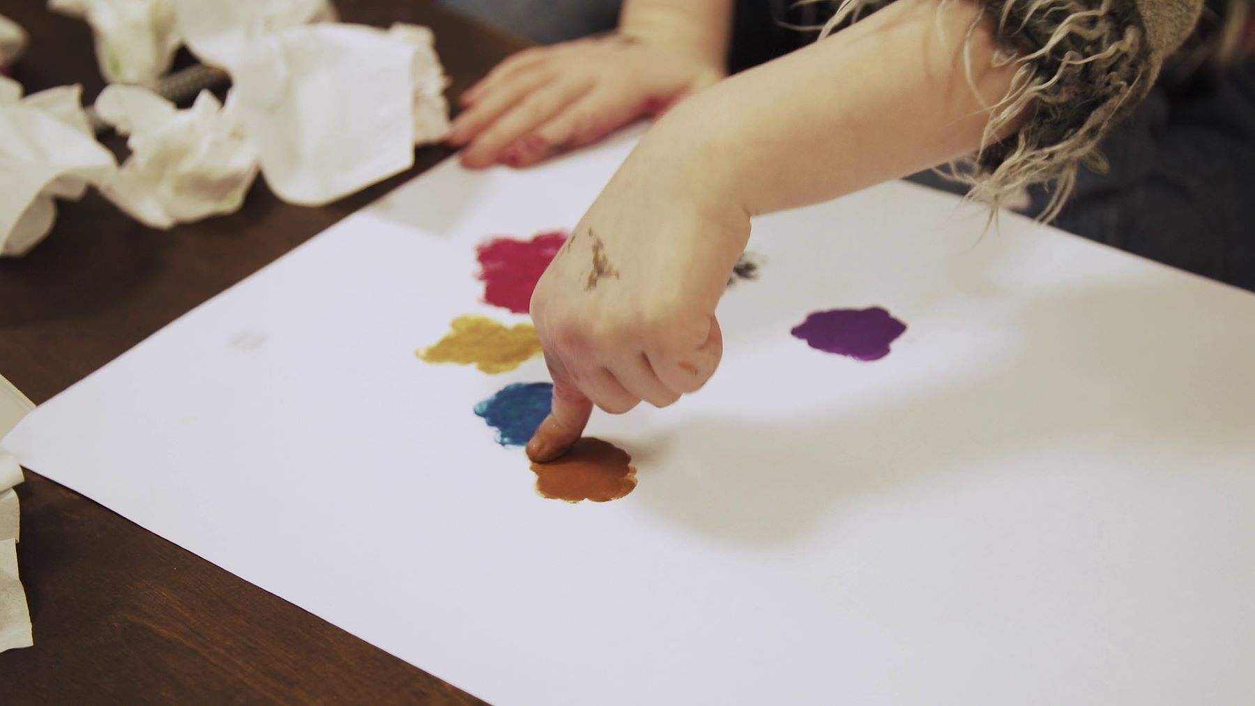 Eine Kinderhand malt Kreise in verschiedenen Farben auf ein Blatt 