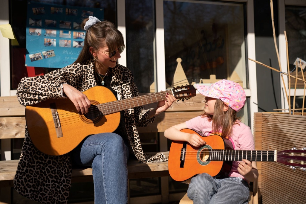 Pädagogische Fachkraft und Kind spielen zusammen Gitarre