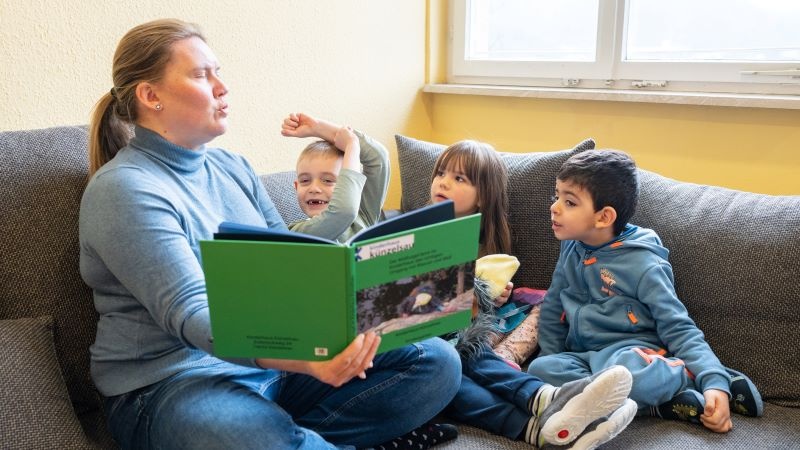 Erwachsene Person schaut mit Kindern in ein Buch
