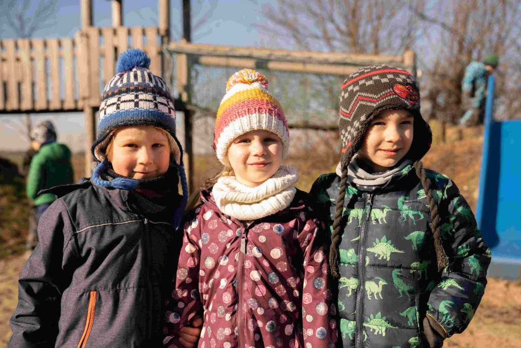drei Kinder mit Jacken und Mützen draußen in der Natur