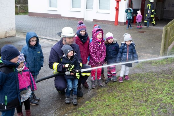 Ein Feuerwehrmann und mehrere Kita-Kinder lassen Wasser durch einen Schlauch spritzen