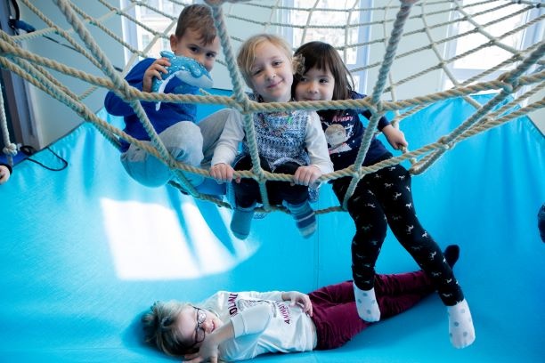 Drei Kita-Kinder sitzen in einem Netz, ein Kind liegt auf einer Matte unter dem Netz