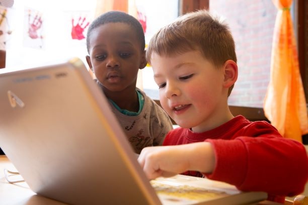 Zwei Jungen sitzen vor einem Laptop und tippen etwas ein
